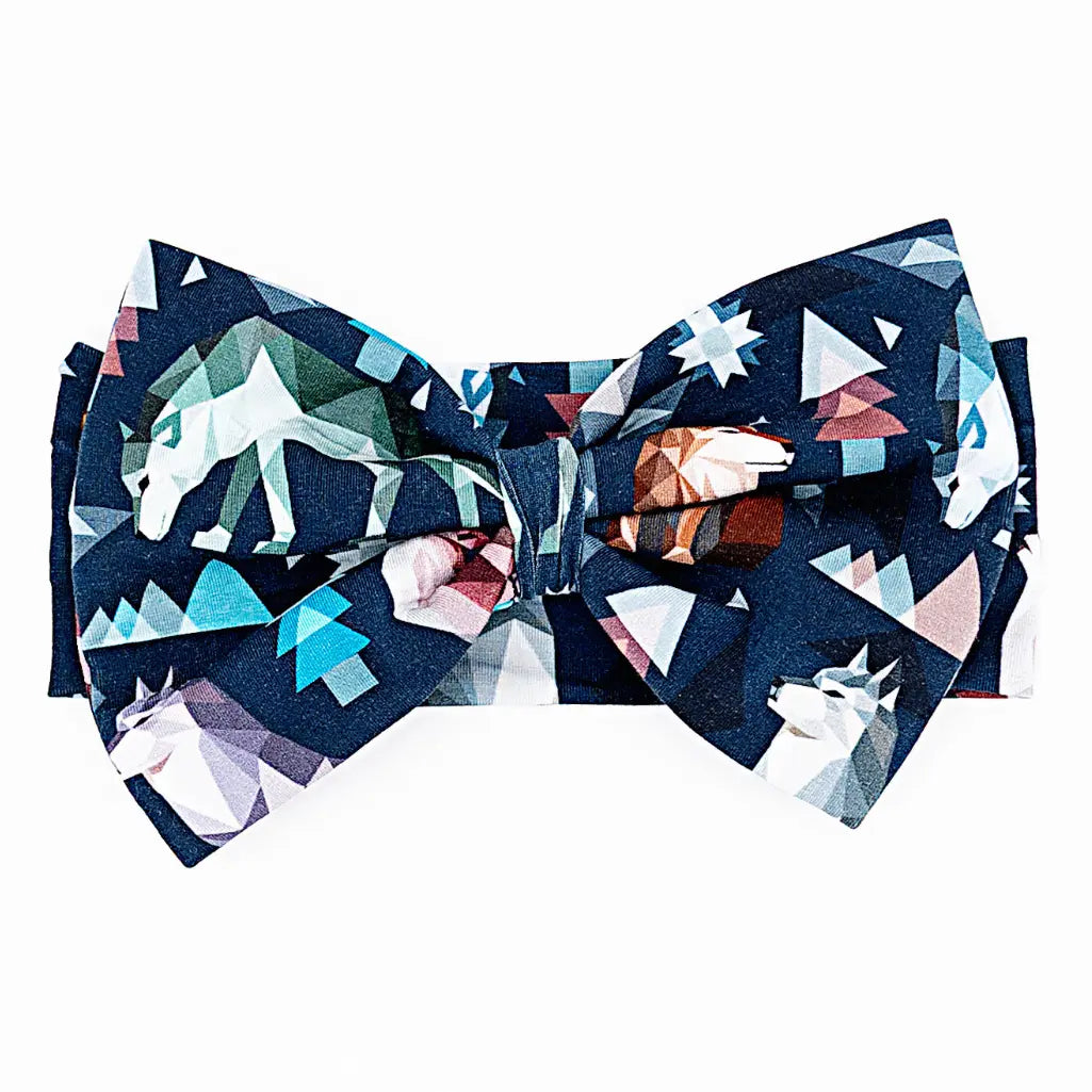 Flat lay of a large fabric bow headband in a navy geometric wolf print with triangle pine trees and snowflakes on a white background.